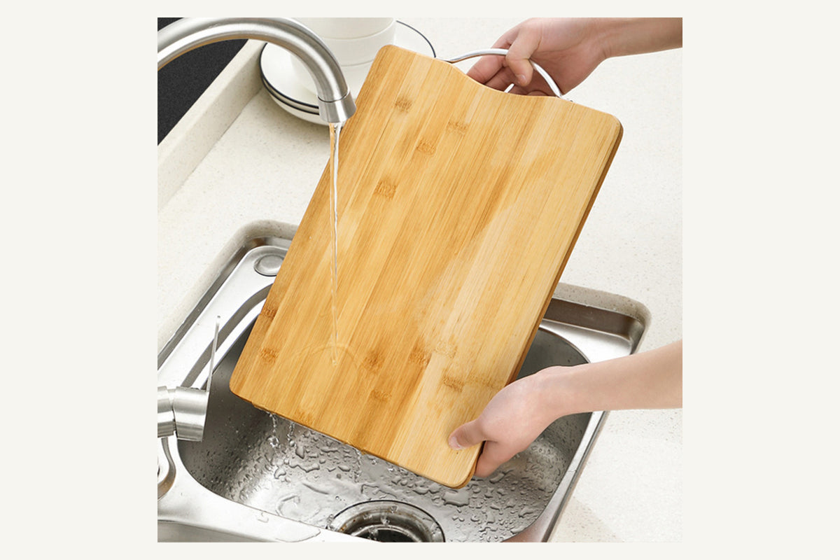 Grove bamboo cutting board being rinsed by hand over a kitchen sink